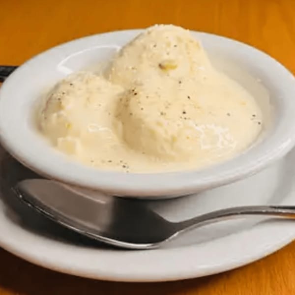 Three scoops of creamy Indian kulfi ice cream in a white bowl with a spoon.