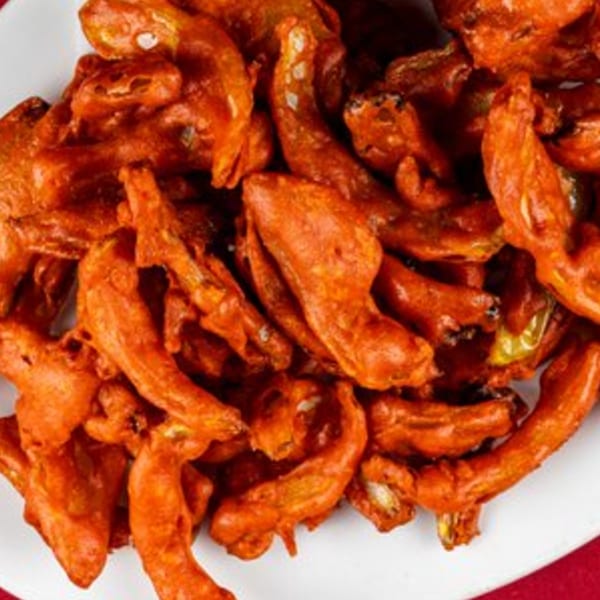 Close-up of a plate filled with crispy, orange-red Indian pakora, a fried snack.