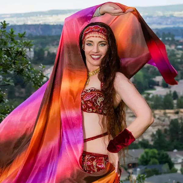 Smiling woman in a red and gold Indian dance costume with a flowing colorful veil outdoors.