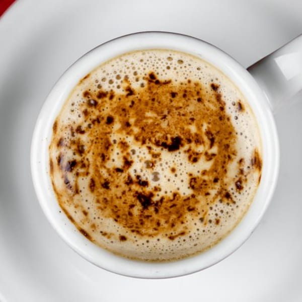 Overhead view of a white cup filled with a frothy, light brown beverage, possibly coffee or chai.