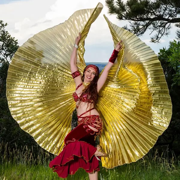 A woman in a red and gold Indian dance costume with large golden wings poses outdoors.
