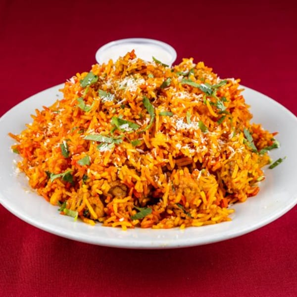 Shri Ganesh chicken biryani, a vibrant orange rice dish with herbs and shredded cheese.