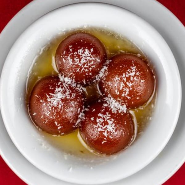 Four gulab jamun, Indian fried dough balls, in syrup topped with shredded coconut in a white bowl.