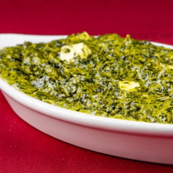Shri Ganesh's Palak Paneer, a vibrant green spinach dish with cubes of paneer cheese, in a white dish.